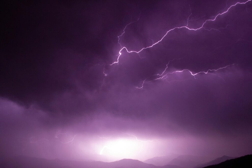 Captivating shot of lightning illuminating a stormy purple sky over a mountainous landscape.